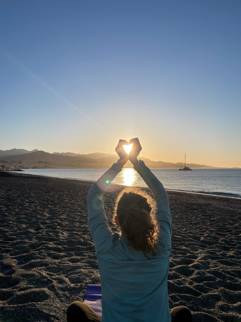 Poranny zachód słońca i Aga na andaluzyjskiej plaży tworząc serce